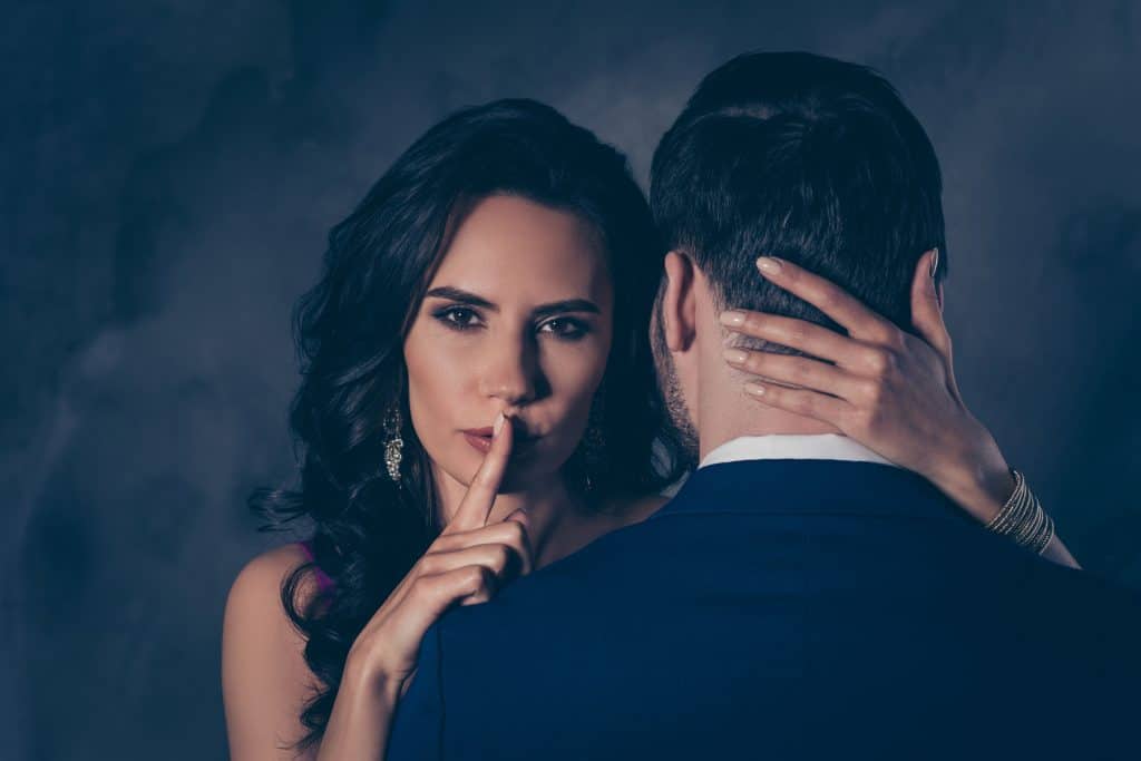 Ssst! Portret van verleidelijke brunette dame die stilte teken toont met wijsvinger die geheime mysterieuze man aanraakt met achteraanzicht, voor een casual date