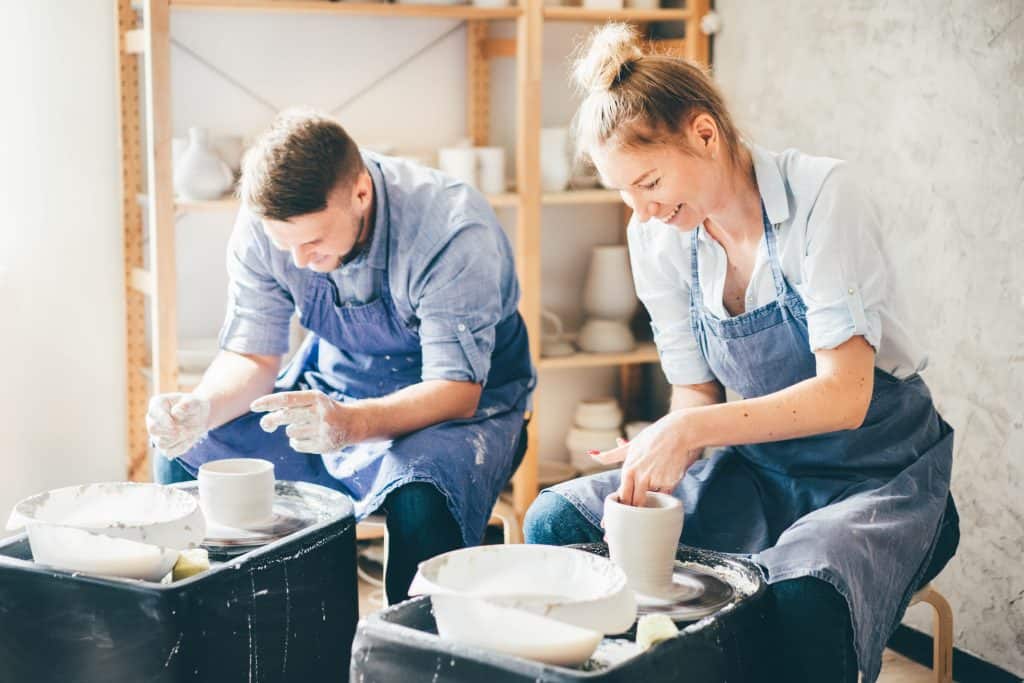 Verliefd stel werkt samen aan een pottenbakkersschijf in hun atelier als leuke Date Ideeën